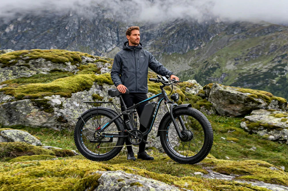 E-BYCCO EB7 Pro fat-tire e-bike with full suspension, parked on mossy mountain terrain with a man standing beside it.