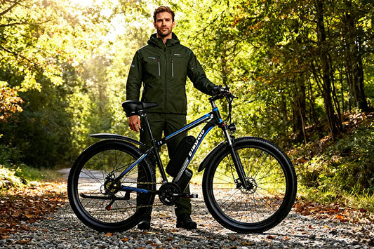 Sun-dappled forest trail lifestyle shot of a male outdoor rider standing beside black-blue E-BYCCO E8 hardtail electric mountain bike on gravel woodland path.
