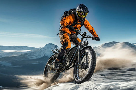 Dynamic winter mountain action shot of rider in orange outdoor gear riding black E‑BYCCO EB7 Pro fat tire electric bike down snowy alpine slopes, kicked‑up snow spray.